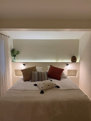 Una cama bien hecha con varias almohadas y un florero sobre una mesita de noche.