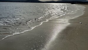 Una playa con un mar tranquilo, un cielo despejado y montañas a lo lejos.