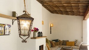 Un interior rústico con una mesa de madera, un tazón de tomates, un farol colgante, un sofá y un suelo de piedra.