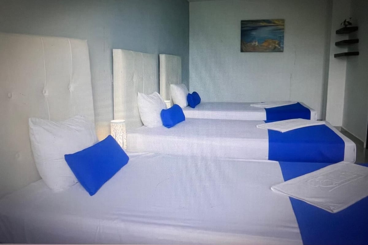 Een hotelkamer met drie bedden, elk voorzien van witte lakens en blauwe accenten.