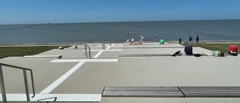 Ein betonierter Weg führt zu einem Strand mit freiem Blick auf das Meer.