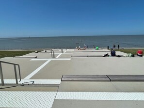 A concrete walkway leading to a beach with a clear view of the ocean.