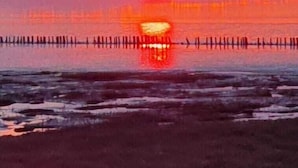 A sunset over a beach with a pier in the distance.