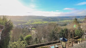 Une vue magnifique depuis un balcon donnant sur une vallée parsemée de maisons et d’arbres.
