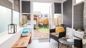 Une terrasse ensoleillée avec un banc en bois, une petite table et un ventilateur.
