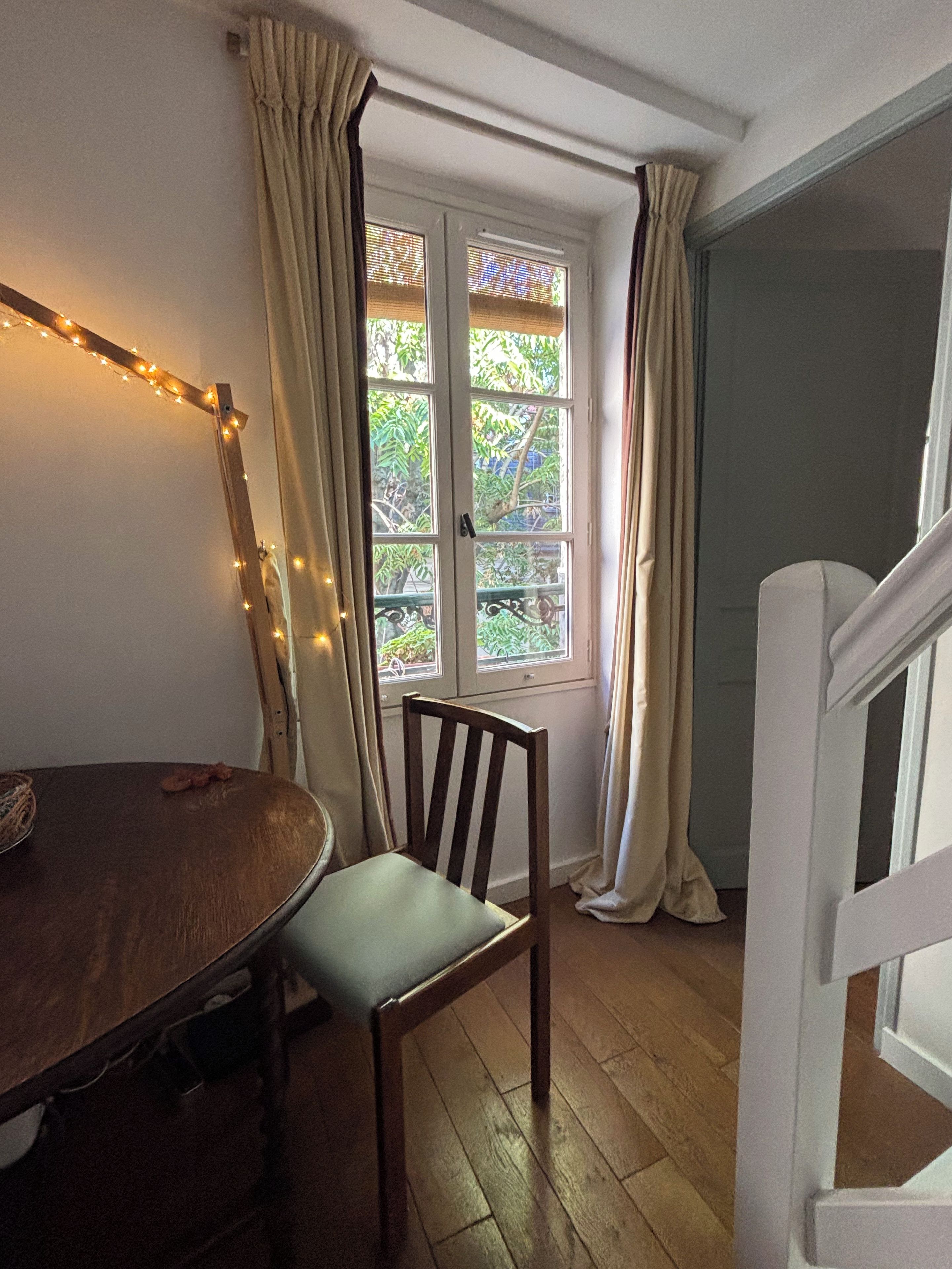 Une pièce comprenant une table à manger en bois, une chaise, une fenêtre avec des rideaux et un escalier.