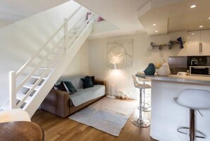 Un apartamento moderno con una escalera, una sala de estar con sofá, una cocina y un pequeño comedor.