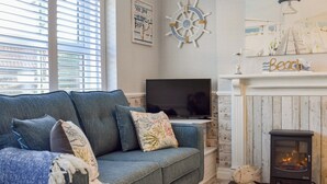 A living room with a blue sofa, a television, a fireplace, and nautical-themed decor.
