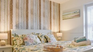 A bedroom with a bed, nightstands, a lamp, a basket of items, and a window with blinds.