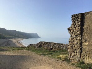 Paisaje costero con un muro de piedra, playa y acantilados.