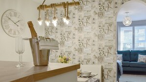 A kitchen with a wooden counter, a clock, a bottle of champagne, and a wall decorated with nautical-themed tiles.