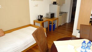 A compact room with a bed, a small table with a kettle, a microwave, and a sink in the background. - Relaxed living in a centrally located apartment (Kleinblittersdorf)