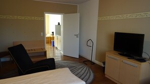 A hotel room with a bed, a TV on a cabinet, a chair, a desk, and a kitchenette in the background. - Relaxed living in a centrally located apartment (Kleinblittersdorf)