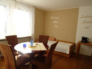 Una habitación con una cama, una mesa con sillas, una botella de agua, una cafetera y una pared con texto.