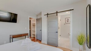 Een slaapkamer met een bed, een nachtkastje, een aan de muur bevestigde televisie en een schuifdeur naar een badkamer.