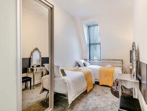 Ein Schlafzimmer mit zwei Betten, einem großen Spiegel, einem Nachttisch, einem Fenster mit Jalousien und einem Teppichboden.