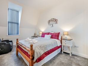 Een slaapkamer met een bed, twee nachtkastjes, een radiator, een raam met jaloezieën, een aan de muur bevestigde decoratie van een boom en een zwarte koffer.