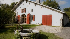 A white building with red shutters and a chimney, a well, and a dog lying on the grass. - Restored farmhouse, fenced garden 1.8 Ha, private swimming pool (Orthevielle)