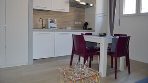 A modern kitchen with white cabinets, a stainless steel range hood, and a dining area with a table and two chairs. - Independent apartment in the heart of the city (Bologna)