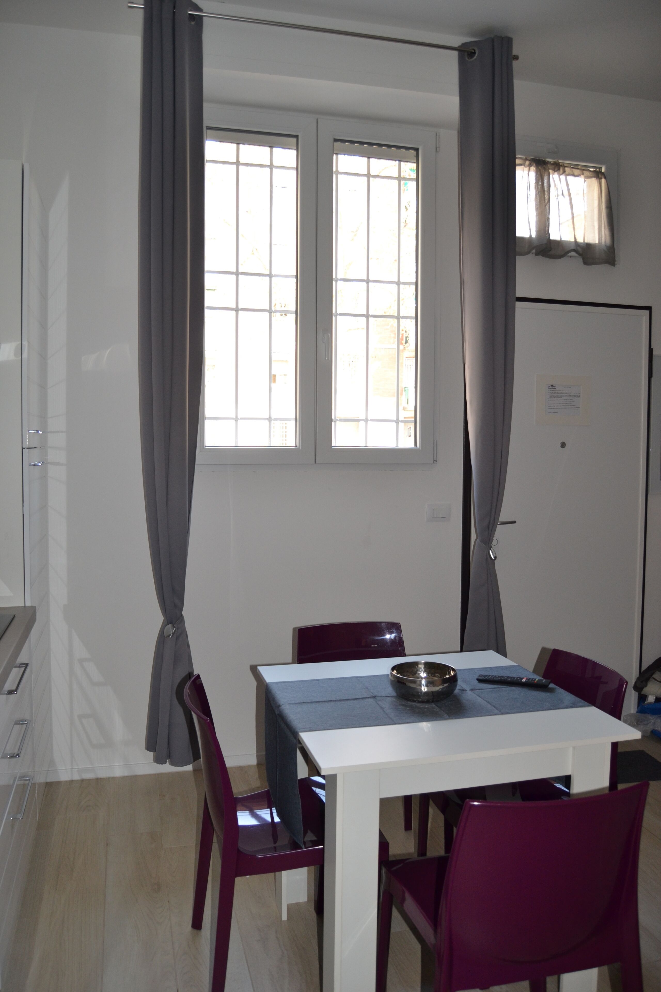 Een eethoek met een witte tafel, paarse stoelen, een schaal en een afstandsbediening.