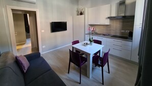 A modern living room with a sofa and a dining table with chairs. There is a kitchen area with cabinets and a TV mounted on the wall. - Independent apartment in the heart of the city (Bologna)