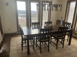 A dining area with a large wooden table and chairs, a woven rug, and a view of a snowy landscape through large windows.