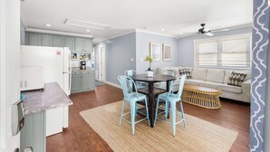 A modern kitchen with light blue cabinets, a dining area with a round table and blue chairs, and a living area with a sofa and a rattan coffee table. - Midtown Beach Escape - Ocean Block | Parking | 3W (Ocean City)