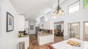 A spacious kitchen with white cabinets, a tiled floor, and a dining area with a table set for two.