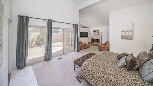 A spacious bedroom with a large bed, a seating area with a fireplace, and a sliding glass door leading to a patio.