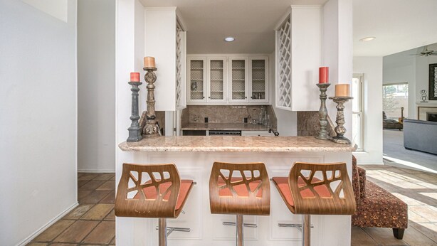 A kitchen with a marble countertop, three wooden bar stools, and two candle holders.