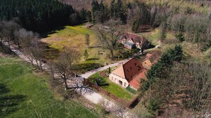 Vue aérienne d’une propriété rurale comprenant une grande maison, une cour clôturée et une forêt environnante.