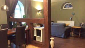 Une pièce comprenant une table à manger en bois, des chaises, un petit meuble blanc, un canapé, une lampe et une fenêtre avec des rideaux.