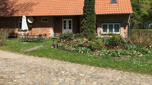 Un bâtiment en briques surmonté d’un toit en tuiles, un jardin fleuri et une allée dallée menant à l’entrée.
