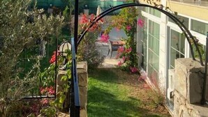 Ein Garten mit einem steinernen Bogen, einer Pergola und Blick auf ein weißes Gebäude mit Balkon.
