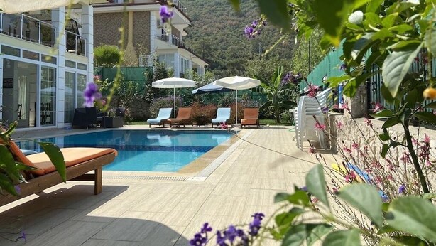 Ein Poolbereich mit Liegestühlen und Sonnenschirmen, umgeben von Grün und mit Blick auf Berge.