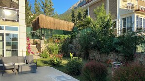 Eine Terrasse mit Gartenmöbeln, einer reetgedeckten Struktur und einem Garten an einer Steinmauer.