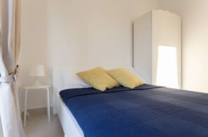 Une chambre à coucher avec un lit, une armoire blanche et une petite table blanche sur laquelle se trouve une lampe.