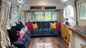 Un intérieur de camping-car chaleureux et confortable, avec un canapé, des coussins, un tapis et une fenêtre agrémentée de rideaux.