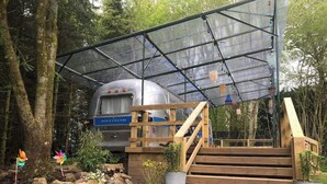Un vieux camping-car est garé sous une structure de toit en métal, et un escalier en bois mène à l’intérieur.