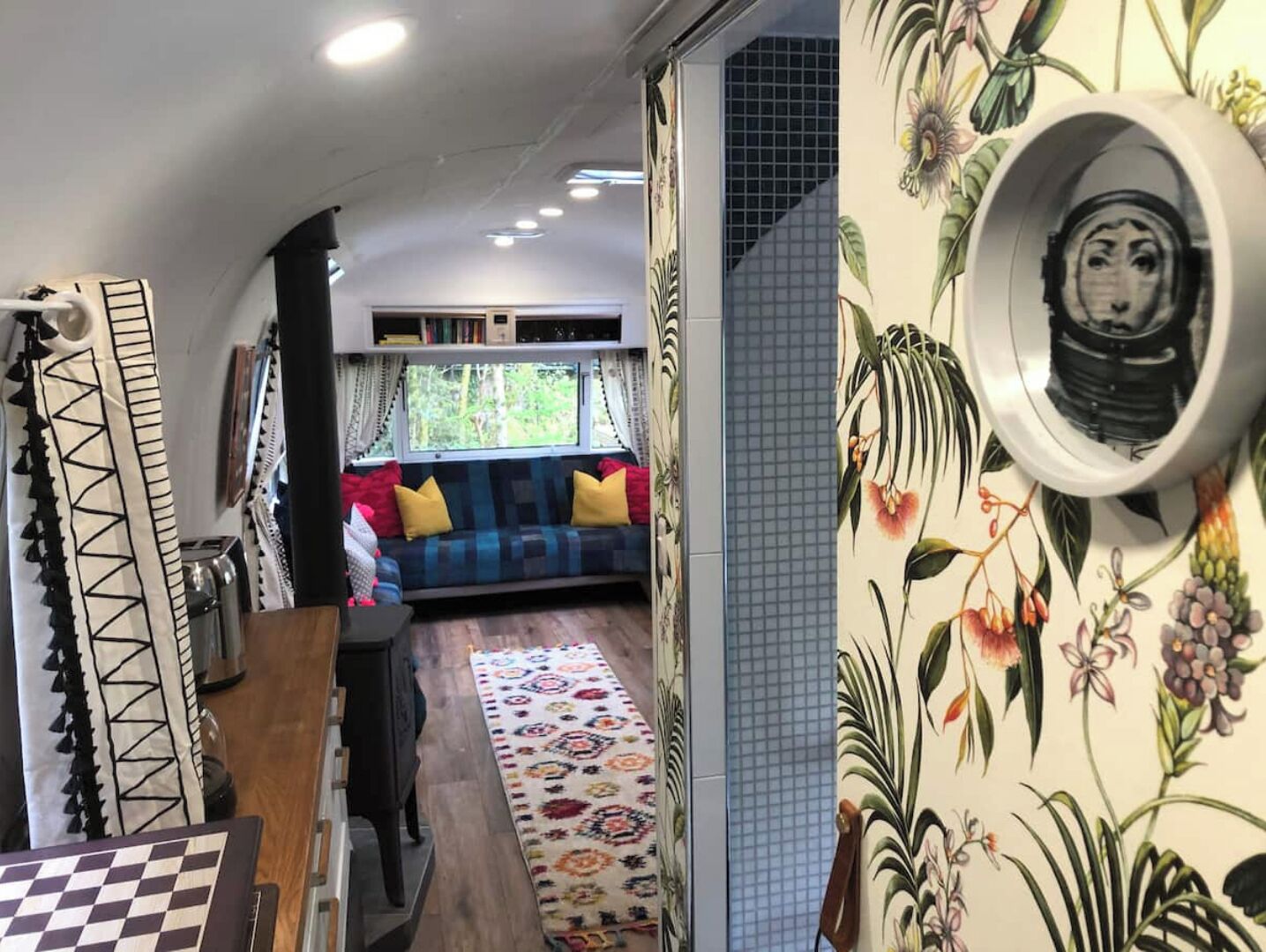 Een gezellig interieur met een bank, behang met een patroon en een raam met uitzicht op groen.