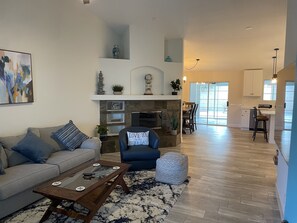 A spacious living room with a fireplace, a dining area, and a kitchen. - Weekend vibes lovely single family home (La Quinta)