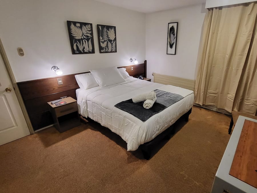 Et hotelværelse med seng, natbord, lampe og et billede på væggen.