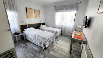 Habitación de hotel con dos camas, un escritorio, una silla, un televisor y una ventana con cortinas.