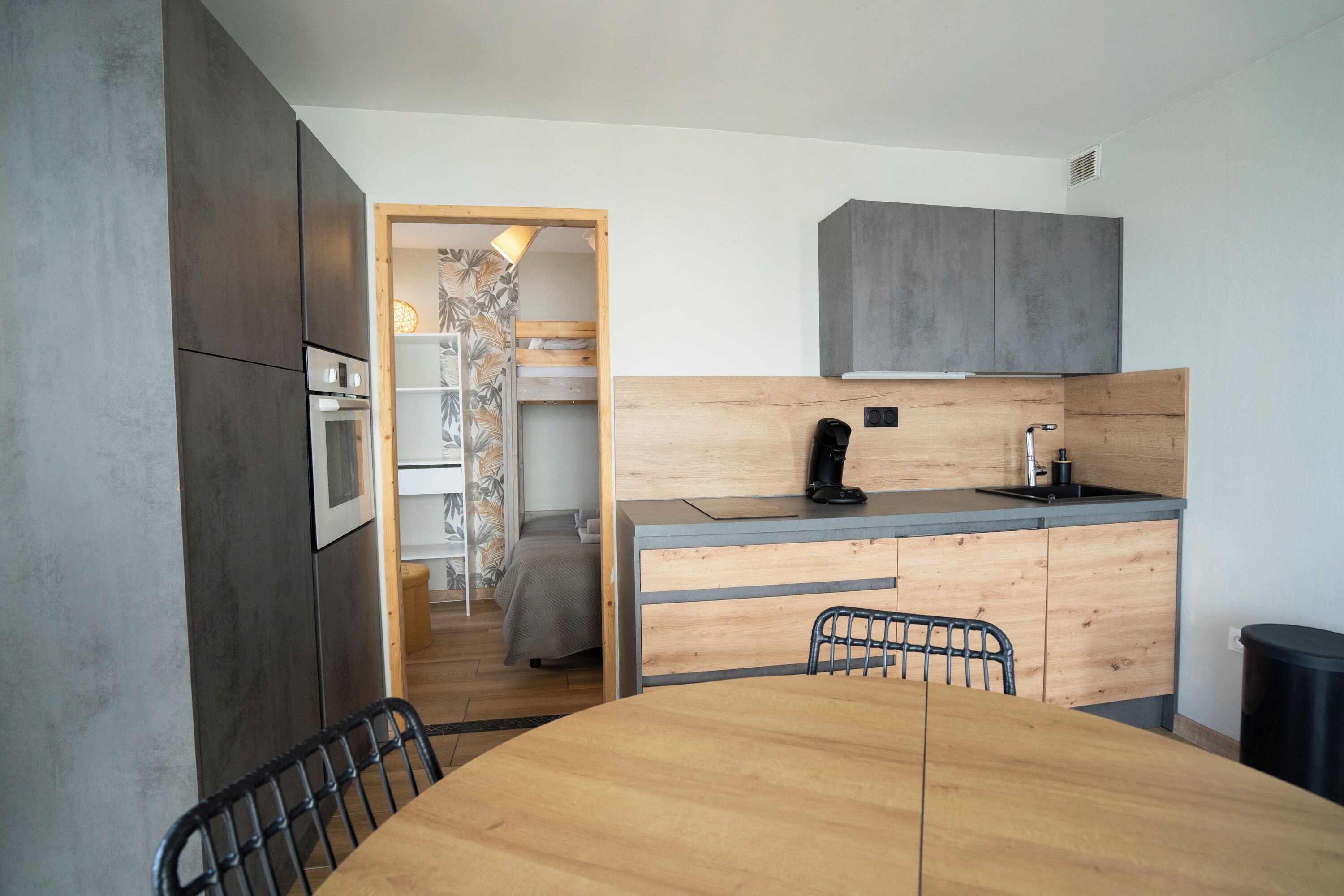 Una cocina compacta con una mesa y sillas de madera, horno empotrado y un lavamanos pequeño.