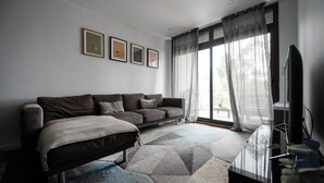 Een moderne woonkamer met een bank, een flatscreen televisie en een groot raam met gordijnen.