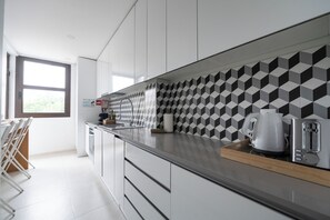 Une cuisine moderne avec des meubles blancs, un pare-feu noir et blanc à motifs et une fenêtre qui laisse entrer la lumière naturelle.