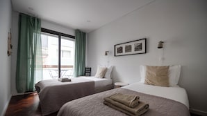 Een hotelkamer met twee bedden, een stoel, een klein tafeltje en een raam met gordijnen.