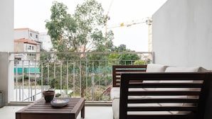 Een balkon met een houten tafel, een plant in pot en een bank.