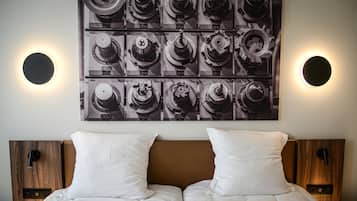 Ein Doppelbett mit weißer Bettwäsche, ein hölzernes Kopfteil und zwei Nachttische mit Lampen. Darüber hängt ein großes Schwarz-Weiß-Foto verschiedener mechanischer Teile.