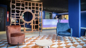 A reception area with a check-in counter, two chairs, a round table, and a geometric patterned floor. - Pegard Andenne Centre (Andenne)